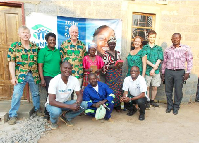 Michael Nugent stands with new Habitat homeowners Failet and Jennifer, local Habitat for Humanity builders and staff, and his teammates, outside one of the two newly built homes in Chipulukusu, Zambia in 2016. © Michael Nugent