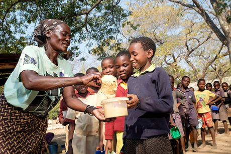 During the Zimbabwe food crisis, a local volunteer cooks and hands out porridge to Surprise (age 10) at a village school where 150kg of healthy corn-soya blend is provided by NGO partners each day. 28/07/16 Photo Credit: Trócaire